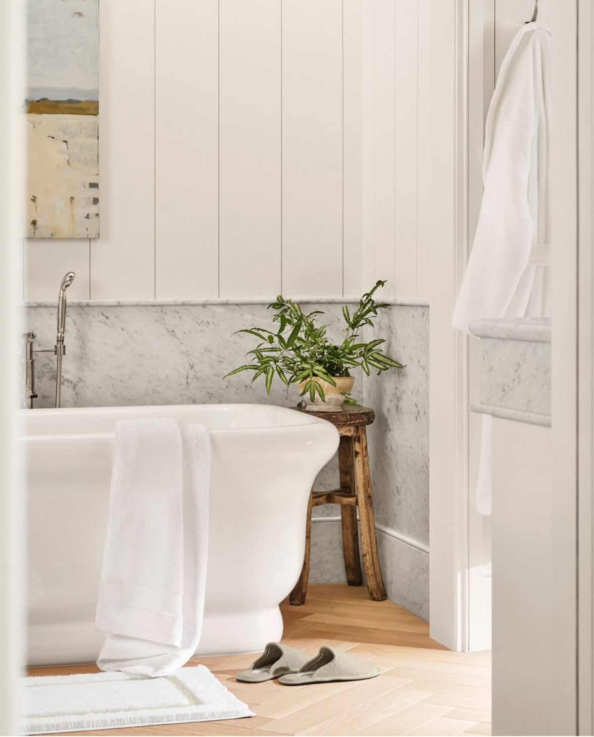 Luxury Bath and Bathroom Essentials. Luxury Bath Towels and linens. A bathtub in a daylight bathroom with a bath mat, a towel hanging over the bathtub, bath slippers, and a bath robe hanging.